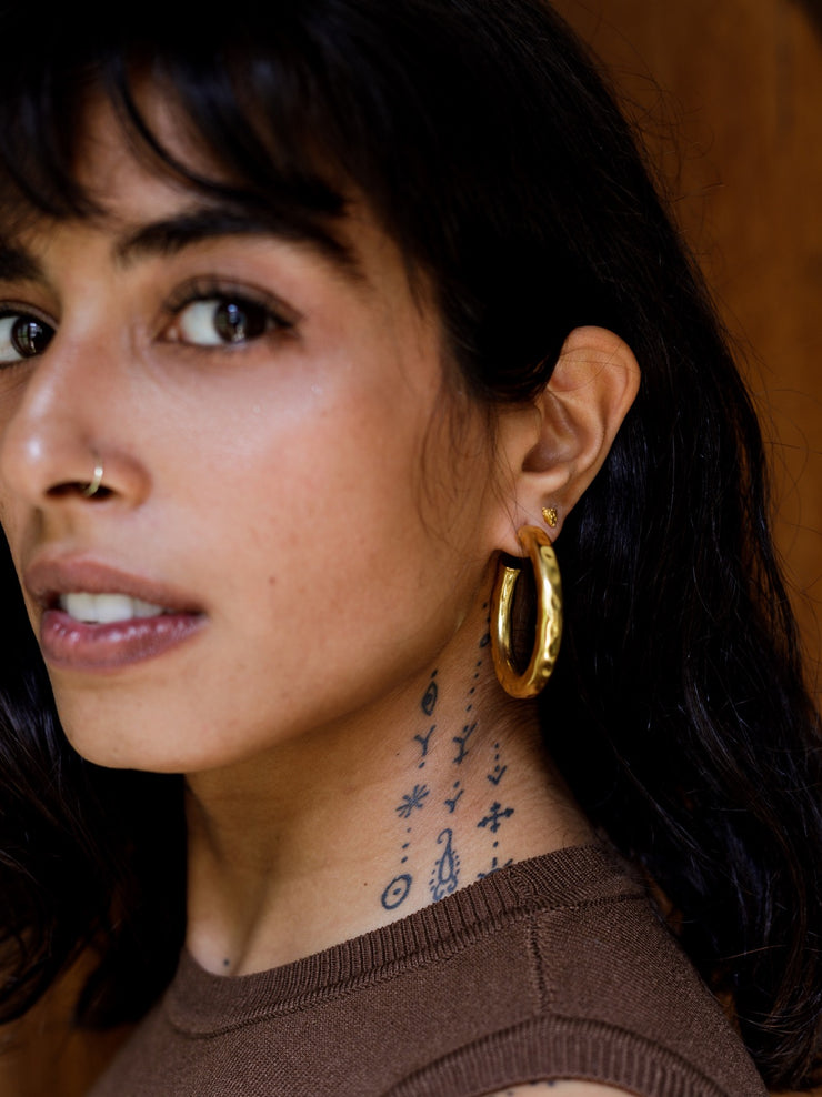 Lightly hammered ripple textured brass with ( one ) 1 micron gold plated medium hoops. Chunky textured hoops that are light-weight and 90s inspired. AM to PM hoops suited for every occasion. Available in 3 ( three ) sizes - small, medium and big.  Armeen wears Medium Ripple Hoops with our teensy Small Illumination Studs
